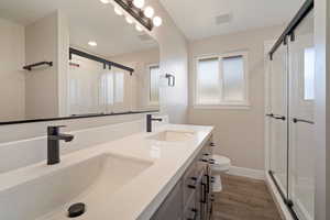 Primary Bathroom featuring wood-type flooring, double-sink vanity, toilet, and a cultured marble shower