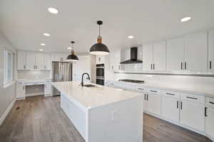 Kitchen with white cabinetry and quartz countertops, an island with waterfall, wall cooktop hood, custom backsplash and stainless steel appliances