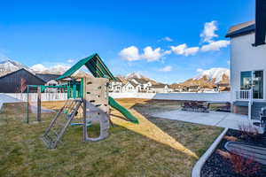 View of playground featuring a lawn, a mountain view, and a patio area