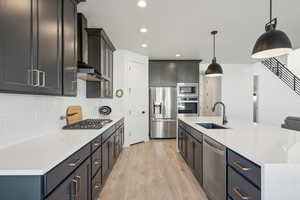 Kitchen with pendant lighting, sink, wall chimney exhaust hood, light wood-type flooring, and appliances with stainless steel finishes