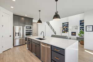 Kitchen with appliances with stainless steel finishes, a kitchen island with sink, sink, light hardwood / wood-style floors, and hanging light fixtures