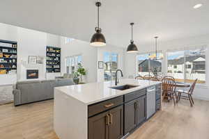 Kitchen featuring sink, stainless steel dishwasher, built in shelves, an island with sink, and decorative light fixtures