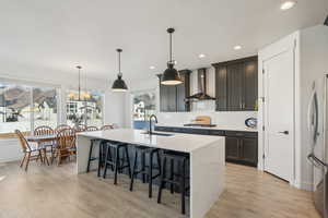 Kitchen with pendant lighting, sink, stainless steel appliances, and wall chimney range hood