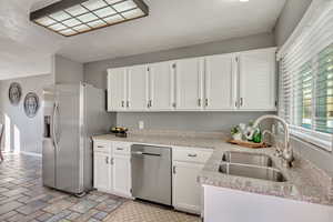 Kitchen with white cabinets, appliances with stainless steel finishes, light stone countertops, and sink