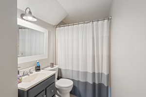 Bathroom with walk in shower, vanity, lofted ceiling, and toilet