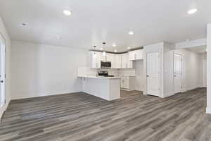 Kitchen with kitchen peninsula, appliances with stainless steel finishes, dark hardwood / wood-style floors, white cabinetry, and hanging light fixtures