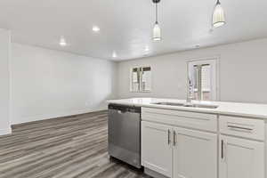 Kitchen with stainless steel dishwasher, sink, white cabinets, dark hardwood / wood-style floors, and hanging light fixtures