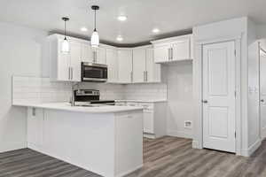 Kitchen with white cabinets, hanging light fixtures, appliances with stainless steel finishes, tasteful backsplash, and kitchen peninsula