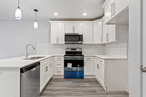 Kitchen featuring white cabinetry, sink, stainless steel appliances, pendant lighting, and decorative backsplash