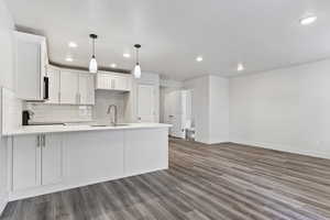 Kitchen with backsplash, white cabinets, sink, hanging light fixtures, and range