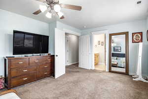 Bedroom featuring ceiling fan, ensuite bathroom, and light carpet