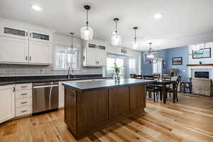 Kitchen featuring stainless steel dishwasher, sink, white cabinets, a center island, and hanging light fixtures