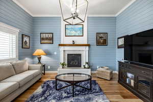 Living room with a notable chandelier, light hardwood / wood-style floors, crown molding, and a brick fireplace