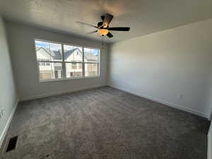 Spare room with dark colored carpet, a textured ceiling, and ceiling fan