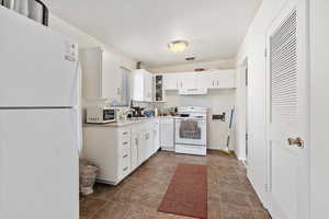 Kitchen with white appliances, white cabinetry, and sink