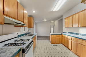 Kitchen featuring light brown cabinets, white appliances, lofted ceiling, and sink