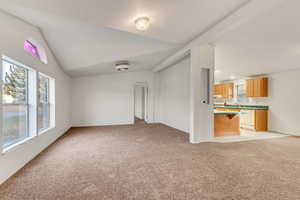 Unfurnished living room featuring light colored carpet and lofted ceiling