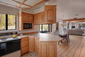 Kitchen featuring decorative light fixtures, a notable chandelier, electric range oven, kitchen peninsula, and black microwave