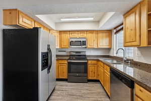 Kitchen with sink, light wood-type flooring, a textured ceiling, appliances with stainless steel finishes, and a tray ceiling