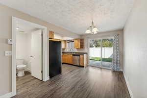 Kitchen featuring dishwasher, dark wood-type flooring, black fridge, sink, and a notable chandelier