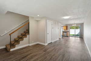 Unfurnished living room with a textured ceiling, dark wood-type flooring, and a chandelier