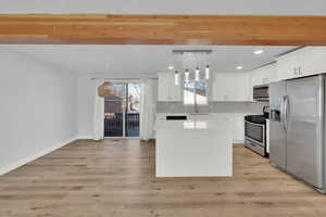 Kitchen featuring white cabinetry, a center island, stainless steel appliances, light hardwood / wood-style floors, and decorative light fixtures.