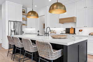 Kitchen with a center island with sink, light stone counters, stainless steel appliances, and white cabinetry