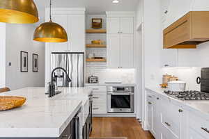 Kitchen with light stone counters, white cabinets, hanging light fixtures, and appliances with stainless steel finishes