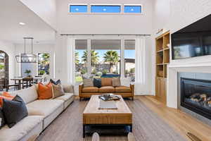 Living room featuring a towering ceiling, a large fireplace, built in features, a notable chandelier, and light hardwood / wood-style floors