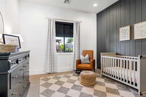 Bedroom featuring light colored carpet, a nursery area, and wooden walls