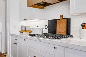 Kitchen with tasteful backsplash, light stone counters, white cabinets, and stainless steel gas cooktop