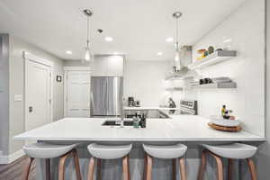 Kitchen with island exhaust hood, appliances with stainless steel finishes, decorative light fixtures, and tasteful backsplash