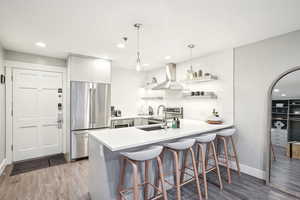 Kitchen featuring kitchen peninsula, stainless steel fridge, tasteful backsplash, island range hood, and white cabinetry