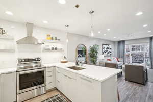 Kitchen featuring stainless steel electric range, sink, wall chimney range hood, and kitchen peninsula