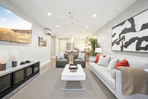 Living room featuring a wall mounted air conditioner, ceiling fan, and wood-type flooring