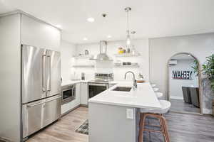 Kitchen with white cabinetry, wall chimney exhaust hood, kitchen peninsula, a breakfast bar area, and appliances with stainless steel finishes