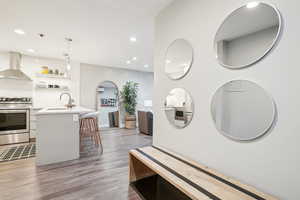 Kitchen featuring sink, wall chimney range hood, stove, a breakfast bar area, and white cabinets