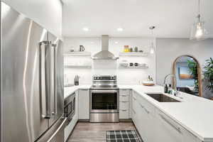 Kitchen featuring white cabinets, hanging light fixtures, sink, range hood, and stainless steel appliances