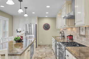 Kitchen with sink, wall chimney exhaust hood, cream cabinets, decorative light fixtures, and appliances with stainless steel finishes