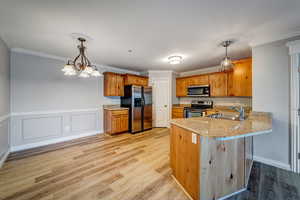 Kitchen with kitchen peninsula, appliances with stainless steel finishes, crown molding, sink, and pendant lighting