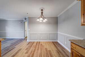 Unfurnished dining area featuring ornamental molding, light hardwood / wood-style flooring, and a chandelier