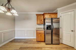 Kitchen with hanging light fixtures, an inviting chandelier, stainless steel fridge with ice dispenser, crown molding, and light wood-type flooring