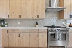 Kitchen with high end stove, tasteful backsplash, and wall chimney exhaust hood