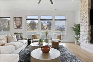 Living room featuring ceiling fan, a stone surround fireplace, and light hardwood floors