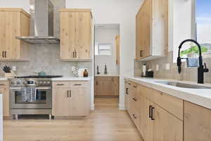 Kitchen with wall chimney range hood, sink, and light brown cabinetry.