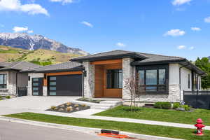 Prairie-style house with stone siding, an attached garage, concrete driveway, a mountain view, and stucco siding