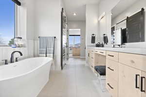 Primary bathroom featuring tile patterned floors, a free standing tub, and double vanity with quartz counter tops.