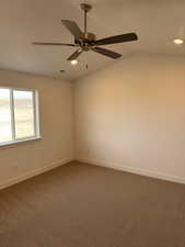 Carpeted empty room with ceiling fan and vaulted ceiling