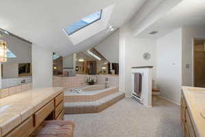 Bathroom featuring a baseboard radiator, lofted ceiling with skylight, toilet, decorative backsplash, and vanity