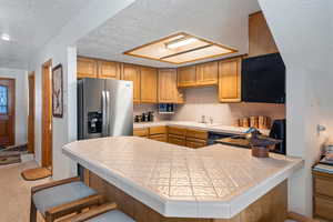 Kitchen with tile countertops, kitchen peninsula, sink, and stainless steel fridge with ice dispenser